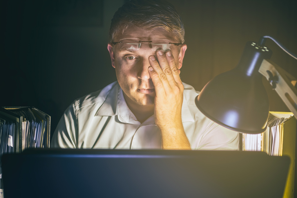 Homem com os olhos cansados devido a muito trabalho na tela do computador.