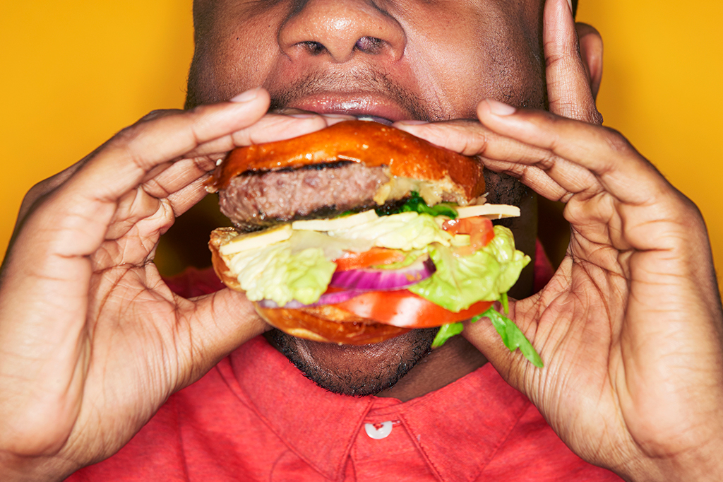 Homem comendo um x-salada bem grandão.