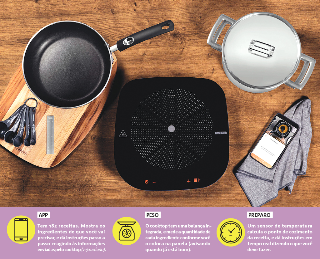 Foto do cooktop Tramontina Guru em cima de uma mesa com duas panelas, um celular, um pano e uma colher de medidas.