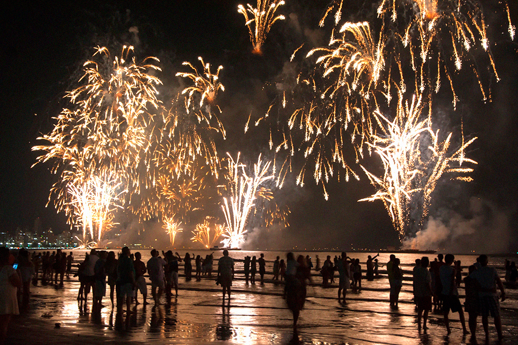Pessoas assistindo aos fogos de artifício à beira da água.
