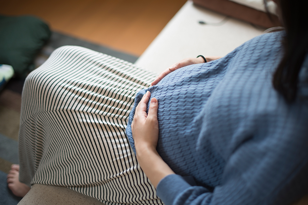 Uma mulher gestante com as mãos repousadas sobre sua barriga.