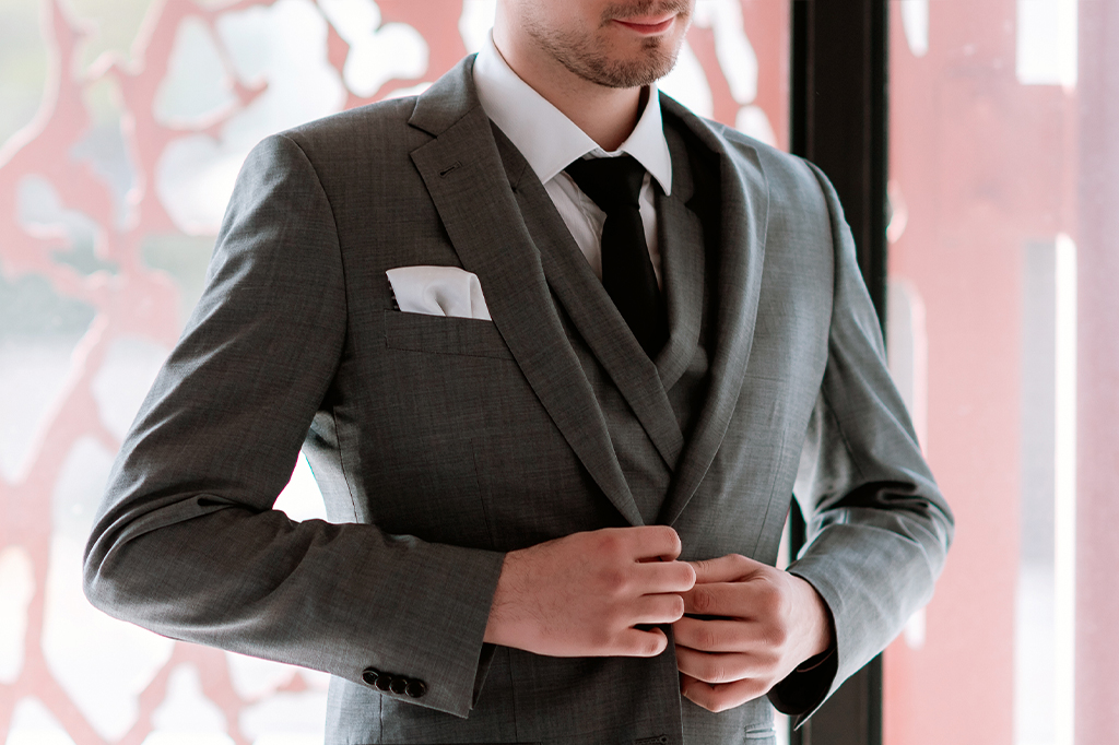 Zoom no terno de um homem, em que vê-se com detalhes o paletó, o colete, a grava e a camisa.