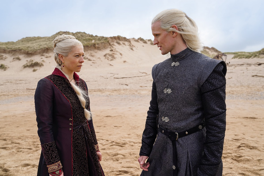 Uma mulher e um homem, respectivamente, na esquerda para a direita, vestindo roupas medievais. Eles estão de frente um para o outro. Ambos possuem cabelos de brancos. Ao fundo o cenário é montanhoso e arenoso.