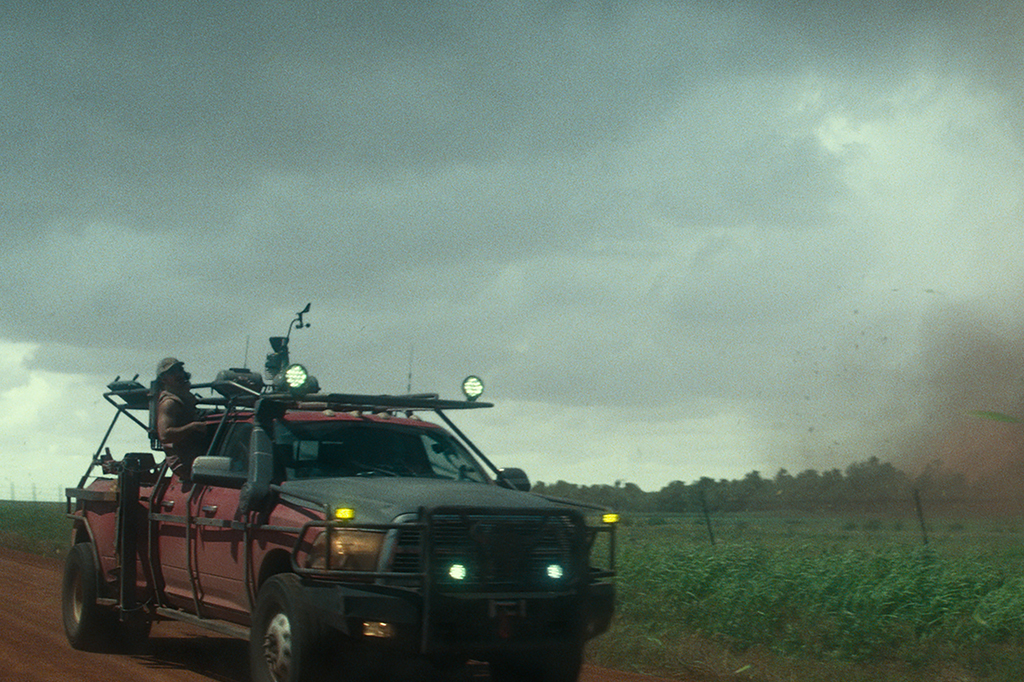 Um homem na janela de um carro. Há um tornado no lado exterior.