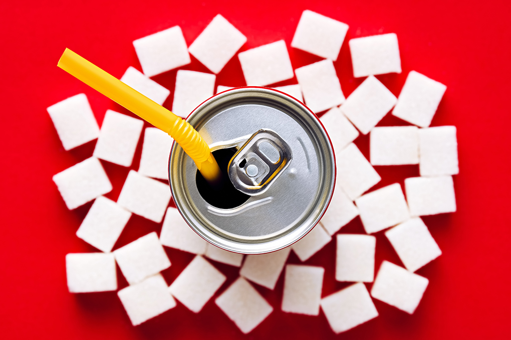 Lata de refrigerante com cubos de açúcar no fundo vermelho.