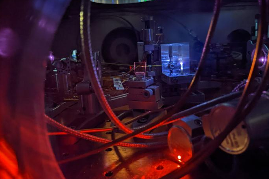 Um poderoso laser brilha em um jato de gás, criando um plasma brilhante e gerando luz ultravioleta. A luz deixa uma linha branca visível ao interagir com o gás restante na câmara de vácuo. Este processo ajuda os cientistas a medir com precisão a energia necessária para excitar o núcleo de tório-229, que é o núcleo de um futuro relógio nuclear.