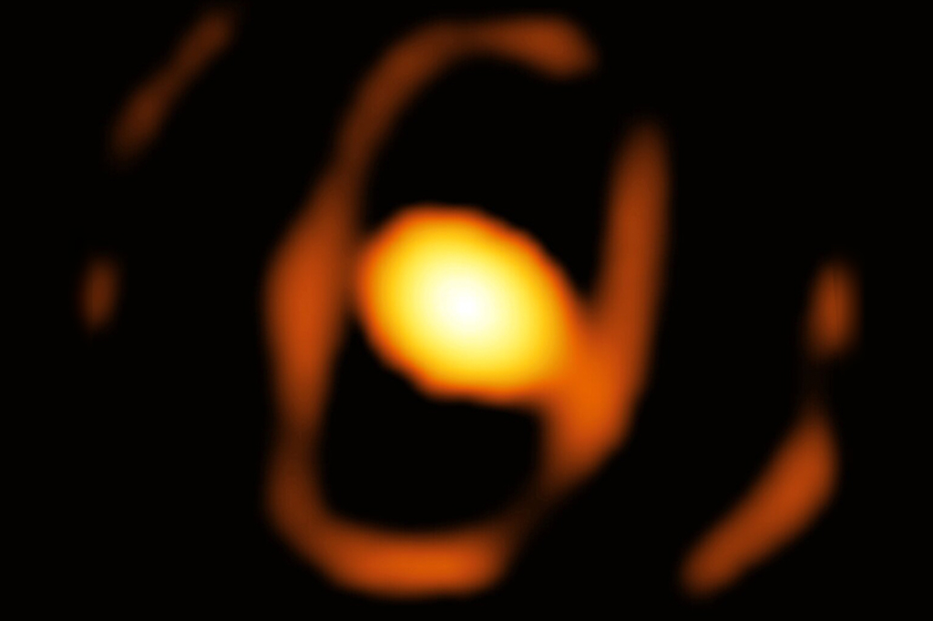 Imagem em close-up de uma estrela fora da nossa galáxia, a Via Láctea. O oval brilhante no centro desta imagem é um casulo empoeirado que envolve a estrela. Um anel elíptico mais tênue ao redor dela pode ser a borda interna de um toro empoeirado.