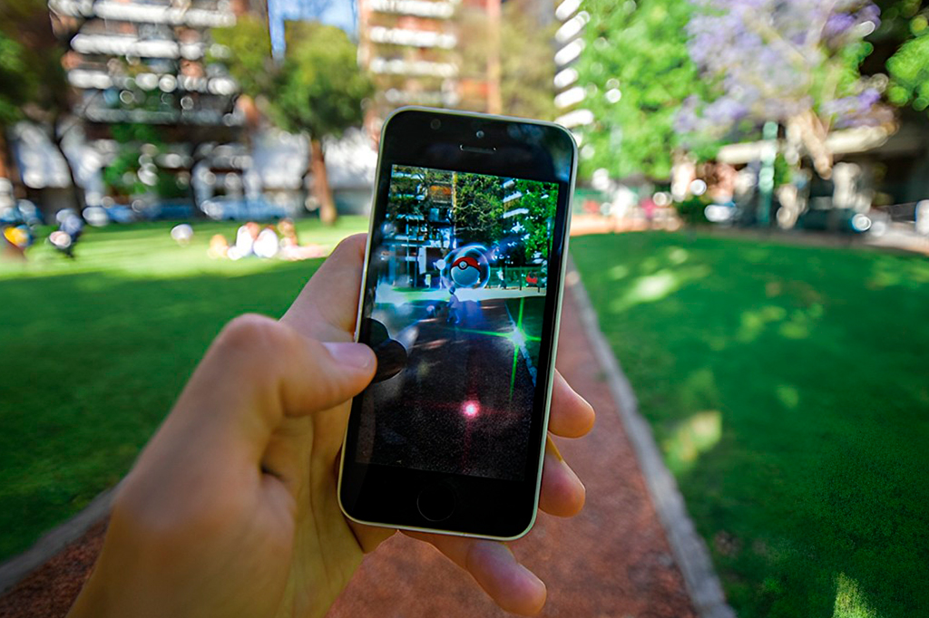 Foto de uma mão segurando o celular, jogando Pokemon-Go.
