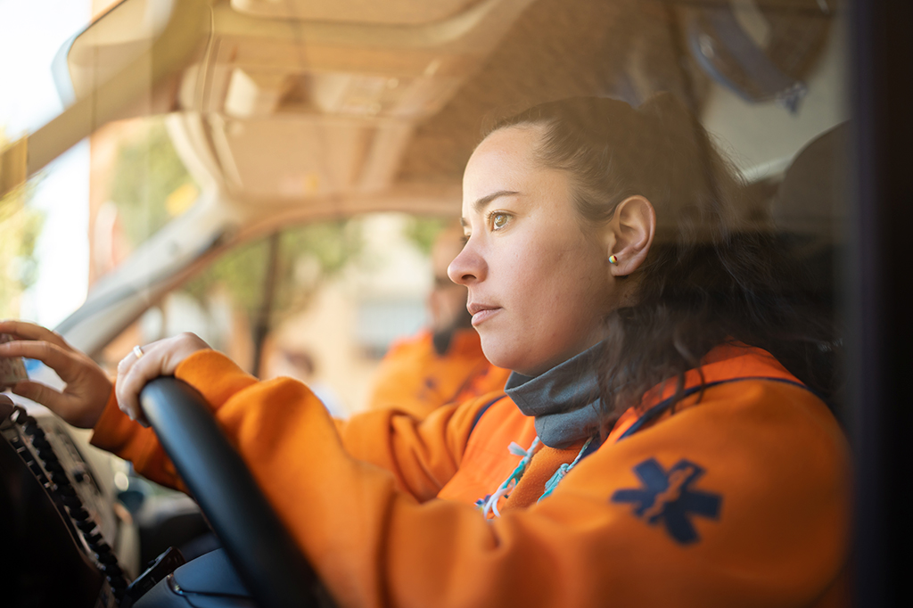 Foto de a mulher observa atentamente enquanto dirige a ambulância. ela está vestida com um uniforme laranja.