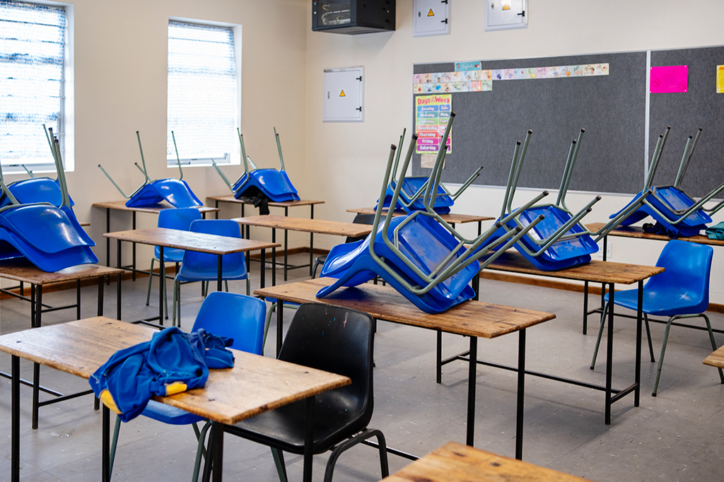 Fotografia de sala de aula vazia com cadeiras sobre a mesa.