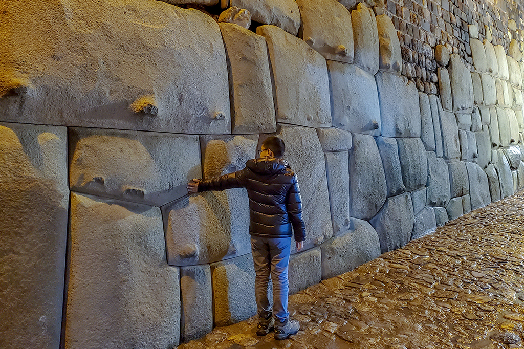 Fotografia da pedra de 12-ângulos. Imagem de um menino com a mão no muro.