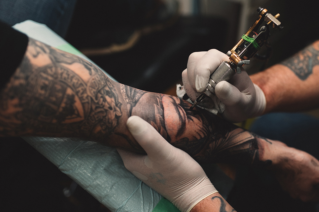 Fotografia de um Tatuador tatuando o braço de um jovem.