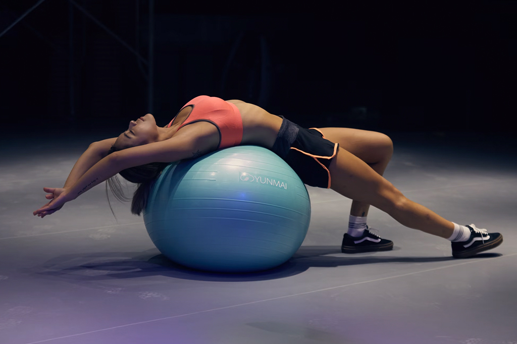 Fotografia de uma mulher fazendo alongamento com um bola de pilates.