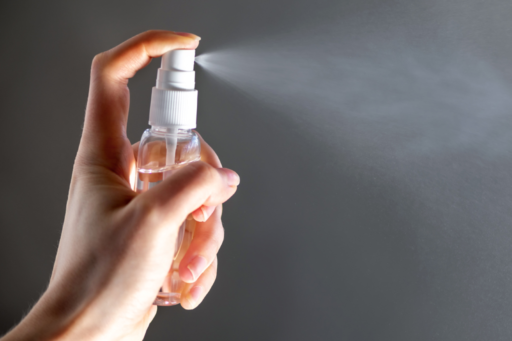 Imagem, em fundo cinza, de uma mão feminina segurando uma embalagem spray de bloqueador de odores.