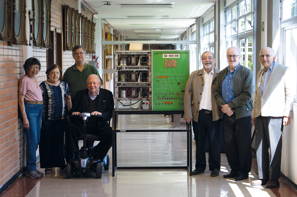 Imagem, de sete pessoas idosas reunidas em torno do antigo computador Imagem do antigo computador LSD &ndash; Pato Feio.