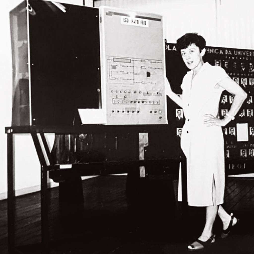 Imagem, em preto e branco, de uma mulher jovem ao lado do computador LSD &ndash; Pato Feio.