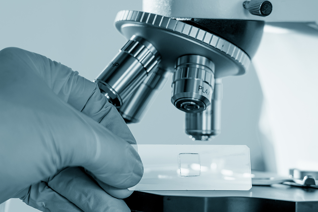 Fotografia de uma mão usando um microscópio.