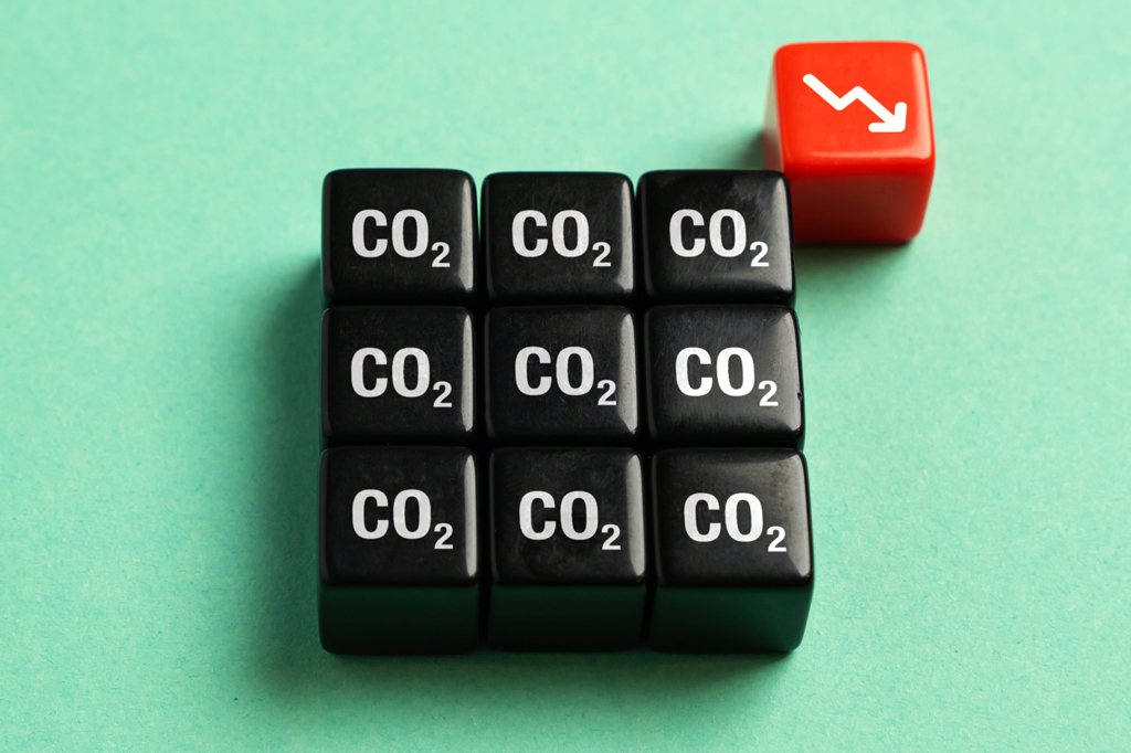 Imagem, em fundo verde, de nove cubos pretos perfilados com a inscrição CO2. No alto, vê-se outro cubo vermelho com uma seta branca apontada para baixo.