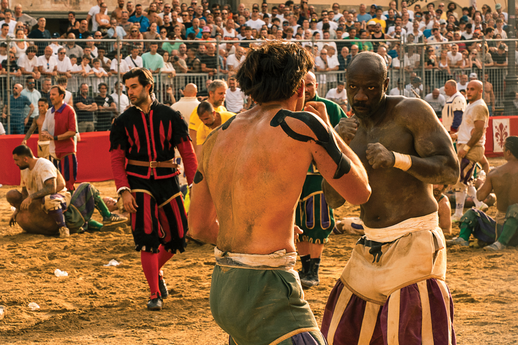 Fotografia de uma cena durante o torneio Calcio Storico Fiorentino de 2025: dois homens lutando numa arena. Ao fundo, vê-se um multidão na arquibancada.
