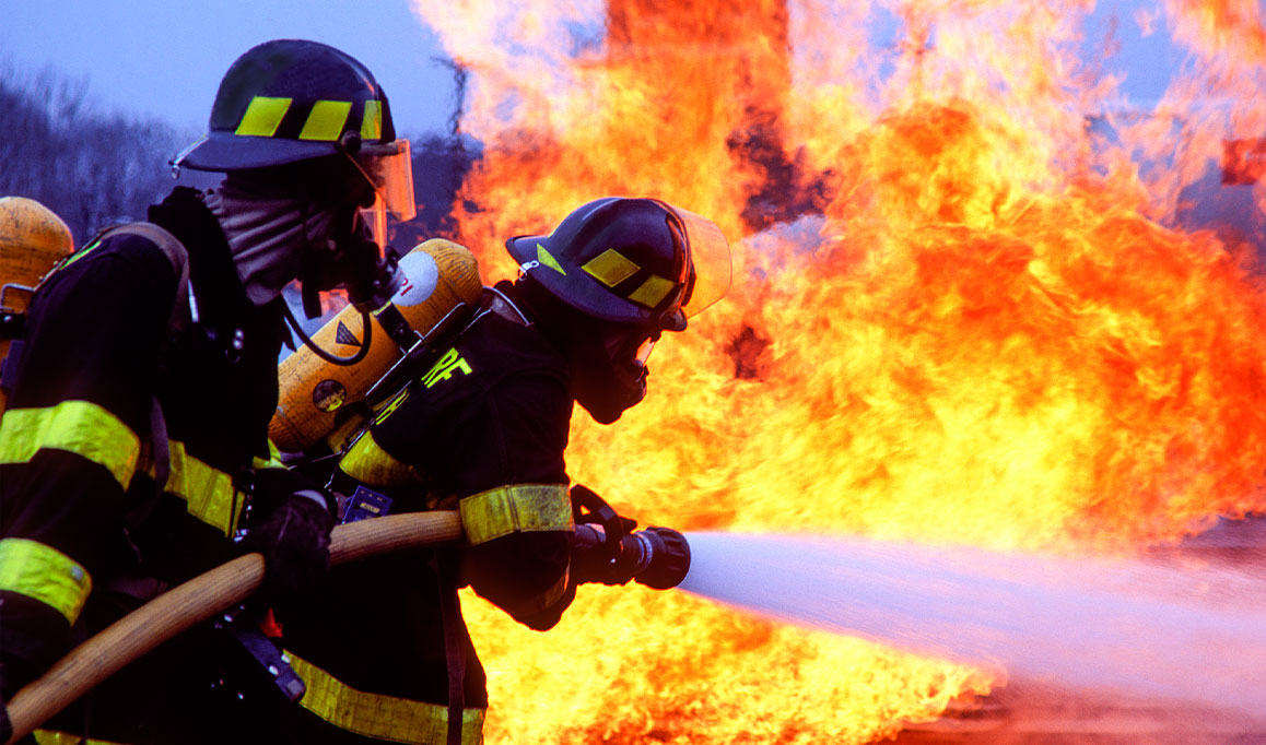 Dois bombeiros apagando incêndio com uma mangueira.