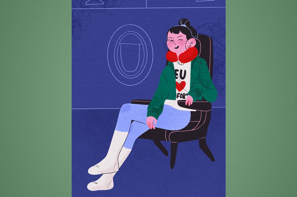 Mulher jovem com coque, usando fones de ouvido, travesseiro de pesco&ccedil;o vermelho, moletom verde e cal&ccedil;a azul, sentada em poltrona de avi&atilde;o com a janela ao fundo.