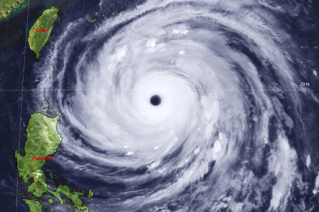 Imagem de satélite mostrando um ciclone tropical massivo com um olho escuro e bem definido, girando sobre o oceano. À esquerda, as ilhas de Taiwan e Filipinas, em verde, são visíveis. Linhas de grade e a marcação 20 N indicam coordenadas geográficas